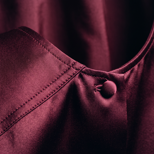 Close detail of deep wine satin at a sculpted shoulder seam with precise topstitching and a covered button