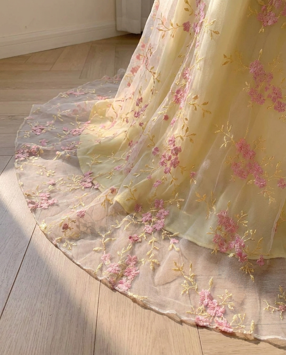 Hem detail of the BIA Élodie Bishop Maxi: the sheer embroidered organza border panel with pink blossoms and gold stems, light passing through it.