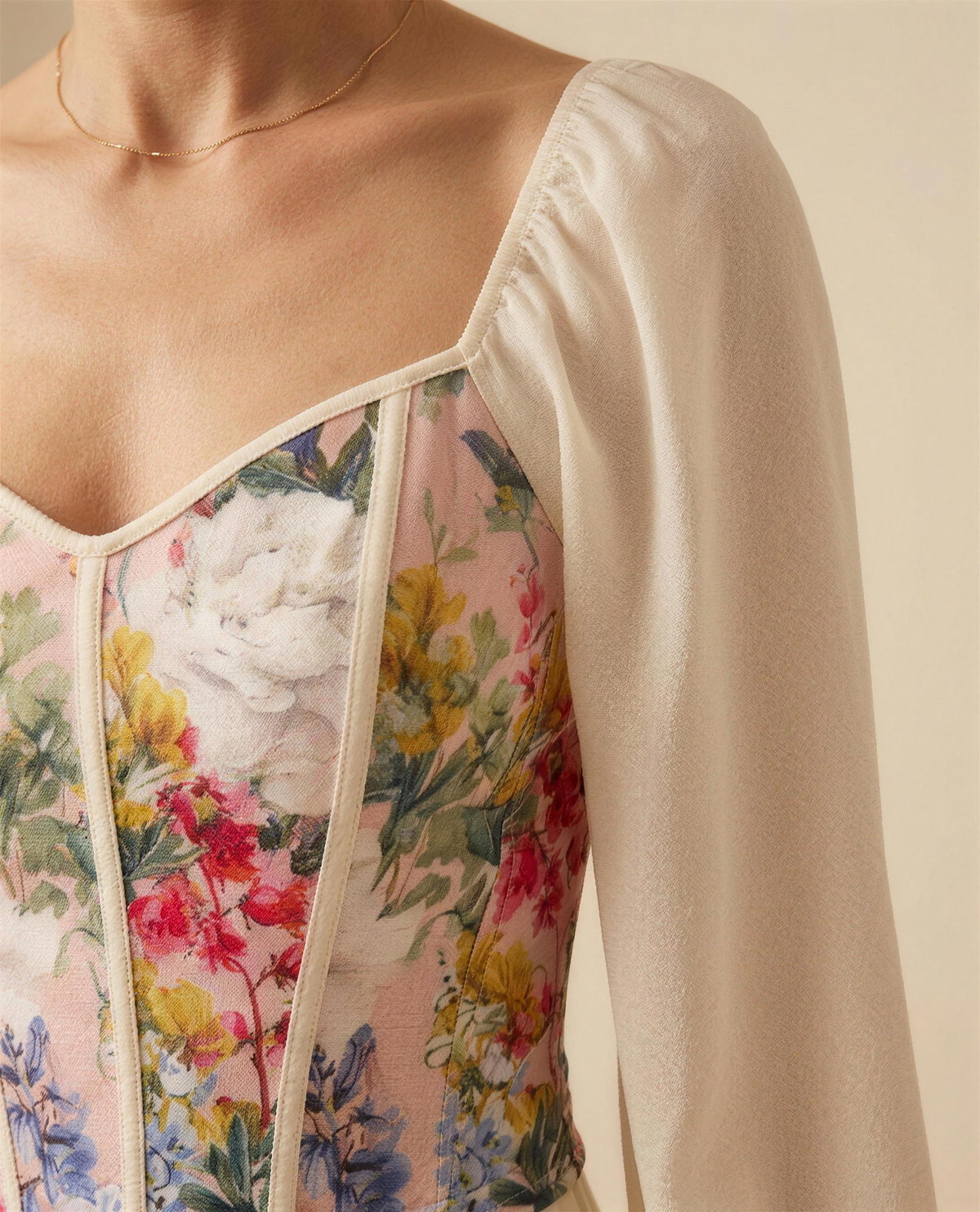 Close detail of the piped panel seams, botanical print and the shoulder point where the cream lantern sleeve is set in