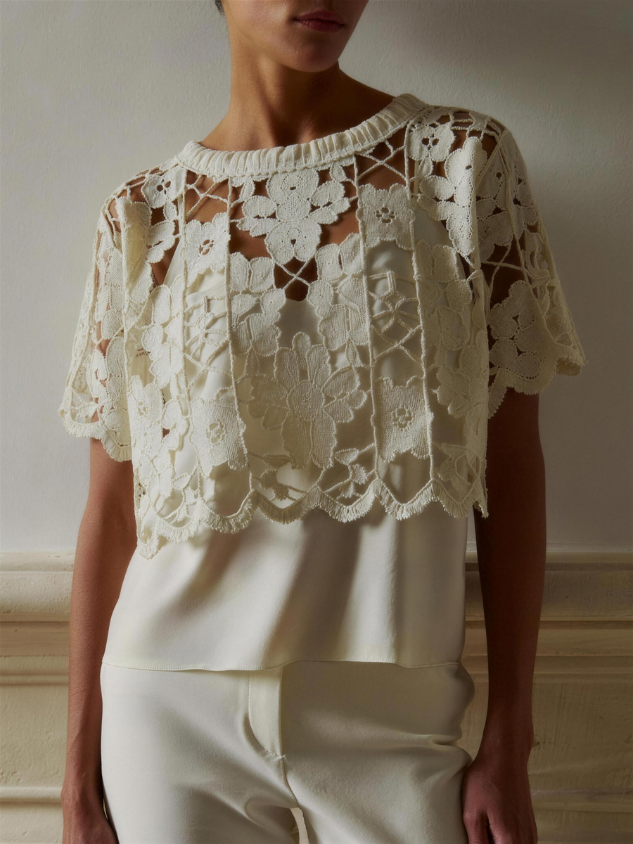 The Coralie Guipure Lace Top in cream, worn layered over a cream silk camisole, showing the raised floral lace, high lace-band neck and scalloped short sleeves