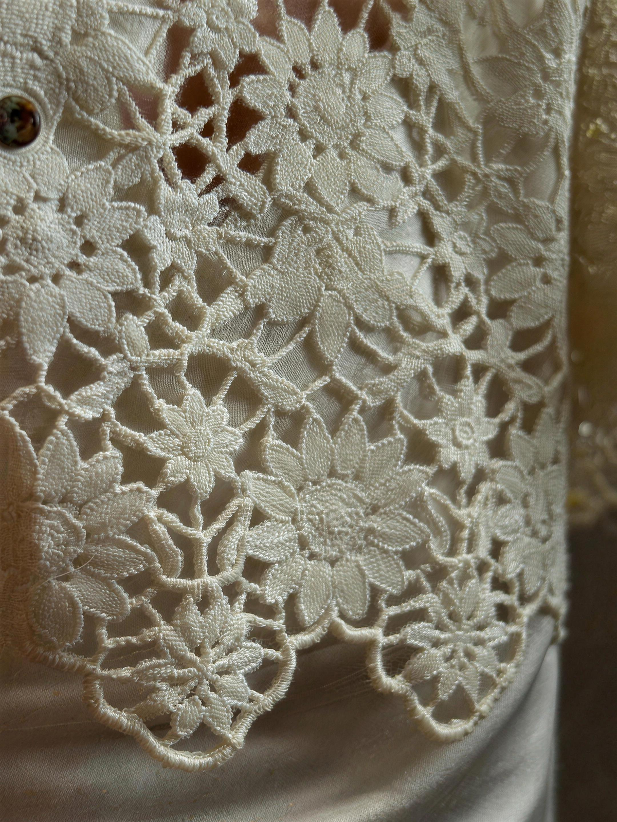 Close detail of the cream guipure lace, showing raised floral motifs joined by narrow bars with open gaps and no net ground, and the scalloped sleeve edge