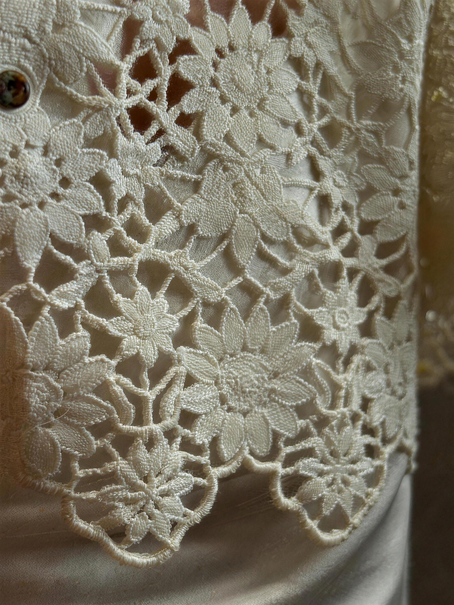 Close detail of the cream guipure lace, showing raised floral motifs joined by narrow bars with open gaps and no net ground, and the scalloped sleeve edge