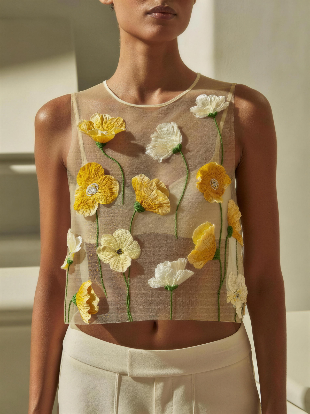 The Amalie Embroidered Floral Top — sheer beige mesh with raised 3D yellow and ivory floral embroidery on green stems, high crew neck, bound armholes, cropped at the waist